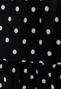 Svart tyg med texturerad yta som har jämnt fördelade vita prickar och en rynkad sömdetalj.