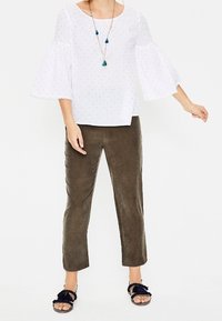 Top blanco con mangas acampanadas que presenta pequeños puntos azules, combinado con pantalones de ante verde oliva y sandalias negras con detalles de volantes.