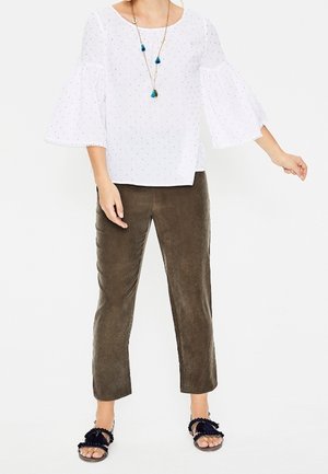 White top with bell sleeves featuring small blue dots, paired with olive green suede pants and black sandals with ruffled accents.