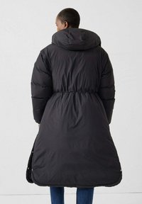 Schwarzer Steppmantel mit tailliertem Schnitt, übergroßer Kapuze und langem Saum. Glatte Textur mit glänzendem Finish und seitlichen Reißverschlusstaschen.