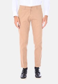Chino beige con una vestibilità slim, dotati di chiusura con bottone e tasche laterali. Indossati con scarpe nere e abbinati a una camicia bianca.