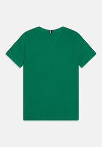 T-shirt corta verde solido con collo a giro, cuciture visibili e un piccolo etichetta rigata nera, bianca e rossa sul colletto posteriore.