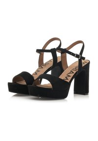 Sandalias de tacón de ante negro con punta abierta, una correa en el tobillo y un tacón alto grueso. Cuentan con una plantilla acolchada y detalles con el logotipo.