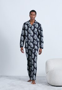 Set di pigiami neri con stampe di tigri bianche, composto da una camicia con bottoni e pantaloni abbinati, realizzato in tessuto morbido con una texture liscia.