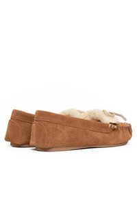 Zapatillas mocasín de ante marrón con un suave forro crema, costuras decorativas y un lazo en la parte frontal. Suela de goma plana.