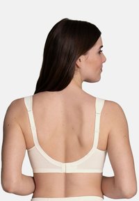 Light beige, seamless bra with adjustable shoulder straps, wide band, and hook closure. Smooth fabric with slight sheen and minimal stitching details.