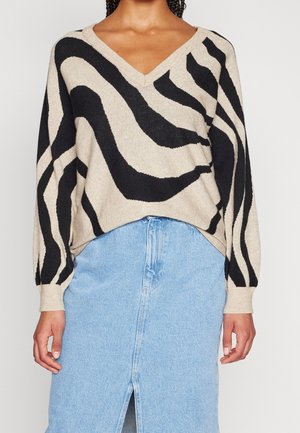 Kvinde iført beige og sort abstrakt stribet V-hals sweater kombineret med en lyseblå denim nederdel med slidse foran.