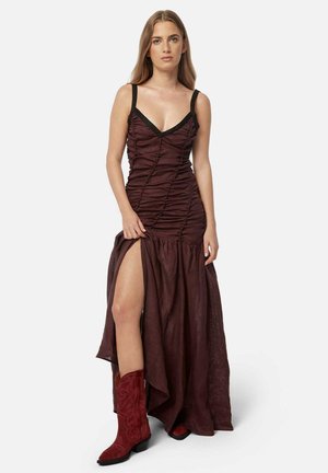 Burgundy maxi dress with ruched texture, deep V-neck, and black straps; features thigh-high slit, paired with red suede cowboy boots.