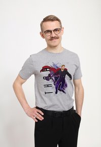 Camiseta de algodón gris con un diseño de superhéroe impreso, que incluye una capa roja y acentos morados. Unos pantalones negros y un cinturón completan el conjunto.
