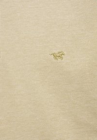 Tissu beige texturé avec un petit logo brodé d'un cheval au galop en fil beige légèrement plus foncé.