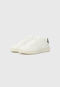 Hvite lær sneakers med en teksturert gummisåle, snøringsdesign og en metallisk detalj på hælen. Glatt overflate og perforerte detaljer.