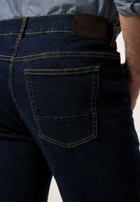 Mörkblå denimjeans med en slät yta, utrustade med gula sömmar, två bakfickor och en brun läderlapp med texten "BOSTON PARK."