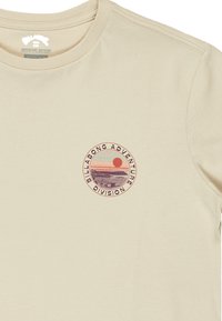 Beige bomulds t-shirt med et rundt grafisk print i nuancer af pink, orange og lilla, med teksten: "Billabong Adventure Division."