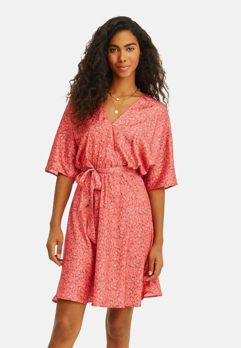 Korálové šaty s krátkým rukávem, s květinovým vzorem, V- výstřihem, páskem v pase a splývavou sukní. Vyrobeno z lehkého materiálu.