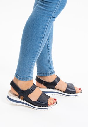 Marineblaue Ledersandalen mit verstellbaren Riemen, strukturierten Akzenten und weißer Gummisohle. Tragen Sie sie zu engen blauen Jeans.