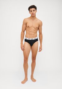 Slip neri con una fascia bianca con il logo "GCDS". Il materiale sembra liscio; il design complessivo è minimale e aderente.