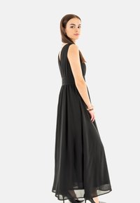 Robe maxi noire avec un corsage ajusté et une jupe fluide, présentant un design à bretelles larges et une texture subtile à la taille. Le tissu lisse tombe élégamment.