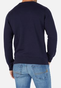 Navyblå sweatshirt med ribbat rundhals och mudd, mjuk textur, bakvy, kombinerad med ljusblå jeans med gula sömmar.