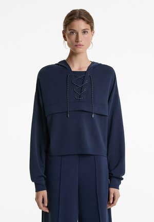 Mörkblå kort hoodie med vida ärmar, snörning fram och texturerad tyg. Matchas med tillhörande byxor med veck.