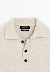 Jasnobeżowy wełniany sweter z prążkowanym kołnierzem, trzema czarnymi guzikami oraz metką z napisem "Massimo Dutti" na szyi. Miękka tekstura, casualowy design.