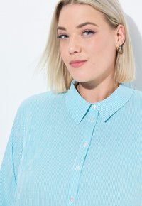 Camicia button-down a righe blu chiaro con colletto classico, caratterizzata da una texture liscia e dettagli dei bottoni ben visibili.