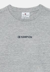 Svetlošedé tričko s okrúhlym výstrihom od značky Champion, s malým čiernym logom Champion umiestneným pod výstrihom.