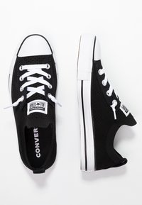 Baskets noires en toile avec bouts en caoutchouc blanc et lacets. Présentent une texture en tricot et un logo sur le côté. Design slim et bas.