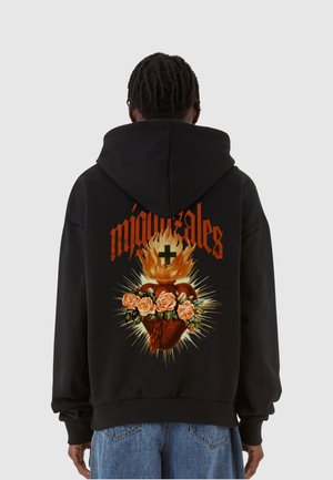 Zwarte hoodie met een grote, kleurrijke hartafbeelding met rozen en vlammen op de achterkant, en vetgedrukte tekst boven het ontwerp.