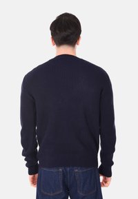 Maglione a coste di colore blu navy con maniche lunghe, collo rotondo e tessuto testurizzato, mostrato da dietro, abbinato a jeans di denim.