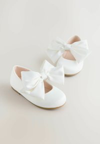 Weiße Ballerinas mit großen Satin-Schleifen vorne, abgerundeter Spitze und weichem Innenfutter; minimalistisches Design mit glatter Textur.