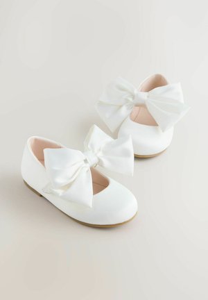 Białe baleriny z dużymi satynowymi kokardami z przodu, zaokrąglonym czubkiem i miękką podszewką; minimalistyczny design o gładkiej teksturze.