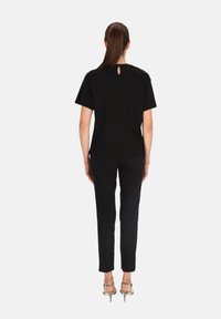 Czarny krótki top z krótkim rękawem i detalem w kształcie otworu z tyłu, zestawiony z czarnymi spodniami o dopasowanym kroju, noszony z beżowymi sandałkami na wysokim obcasie.