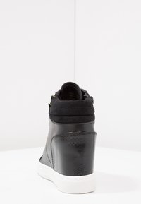 Black sneaker with a textured leather and suede upper, high-top design, white rubber sole, and zip closure at the back.