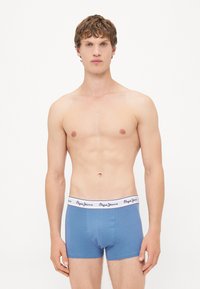Boxeri scurți din bumbac albastru, cu un brâu elastic alb ce prezintă brandul negru "Pepe Jeans", purtați de o persoană cu părul scurt.