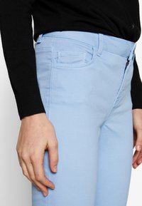 Ljusblå bomullsjeans har en tajt design med dragkedja och knappstängning, kompletterat med en bakficka och subtila sömnadsdetaljer.