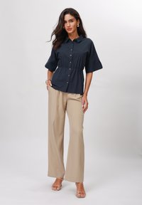 Camicetta navy a maniche corte con bottoni e vita peplum, abbinata a pantaloni beige a gamba larga. Tessuto liscio, design minimalista.