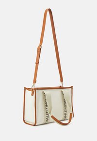 Tote bag en toile crème avec des accents en cuir marron, présentant un détail de logo central en bande et une bandoulière en cuir ajustable.