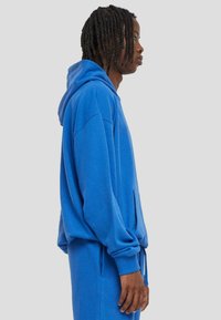 Blauwe hoodie gemaakt van zachte stof, met een zak aan de voorkant en lange mouwen, gestyled met een losse pasvorm.