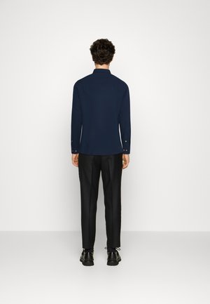 Navy long-sleeve shirt with a collar, featuring button cuffs, paired with black tailored pants and black shoes, shown from the back.