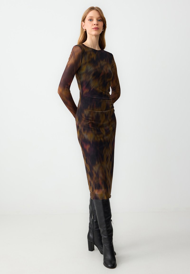 Langsleeve, getailleerde jurk in een bruin en zwart tie-dye patroon, met een soepele textuur. Gekoeld met kniehoge zwarte laarzen.