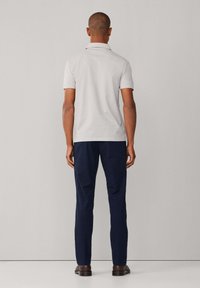 Polo gris de manga corta combinado con pantalones azul oscuro. El modelo está de espaldas a la cámara, mostrando la tela suave y el diseño sencillo.