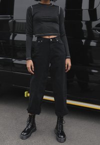 Zwarte cropped langemouwen top met contrasterende stiksels, gecombineerd met hoge taille zwarte wijde pijpen broek en zwarte veterschoenen.