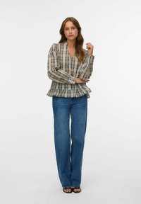Blusa a quadri con maniche a sbuffo, scollatura a V e orlo arricciato, abbinata a jeans a gamba dritta di colore azzurro chiaro e sandali neri.
