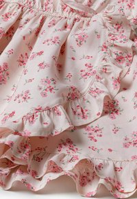 Blumenbekleidungen aus einem sanften rosa Stoff mit kleinen roten und grünen Blumen, einer gerafften Taille und geschichteten Rüschensaum.