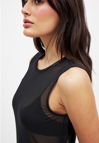 Top senza maniche nero con un design a pannello trasparente, tessuto morbido e scollatura a girocollo classica, che mette in risalto una silhouette aderente.
