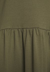 Robe vert olive en tissu doux, avec une couture à la taille froncée et une partie inférieure fluide ornée de plis pour plus de texture.