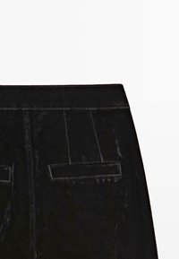 Section de jupe en cuir noir montrant la ceinture, les coutures verticales et deux fausses poches arrière horizontales avec détails de couture.