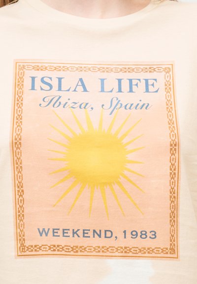 Κίτρινος ήλιος με ακτίνες μέσα σε κάδρο με μπεζ και πορτοκαλί σχέδια, το κείμενο γράφει "ISLA LIFE Ibiza, Ισπανία Σαββατοκύριακο, 1983" σε ανοιχτό ύφασμα φόντο.