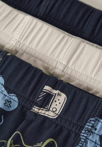 Dwie pary bokserek chłopięcych: jedna granatowa z kreskówkowymi wzorami i zielonymi akcentami, druga beżowa, obie z elastycznymi pasami w talii.