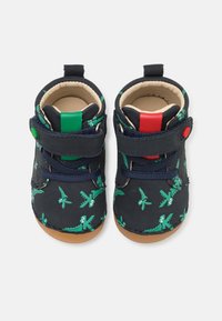 Chaussures bleu marine avec des motifs de crocodile vert et d'avion, dotées de bandes auto-agrippantes, d'une semelle texturée et d'accents colorés sur le talon.